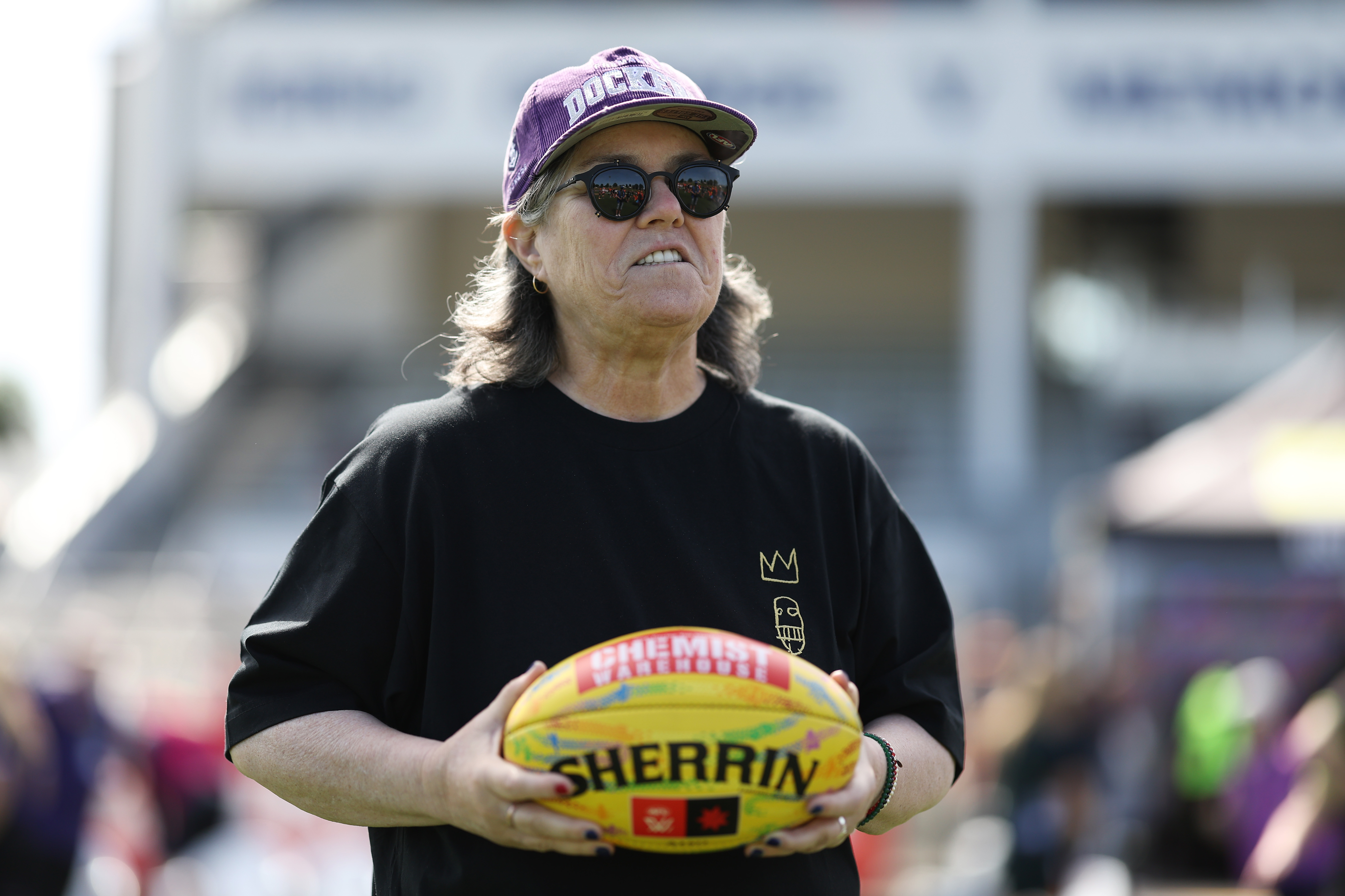 Rosie O'Donnell holding an Australian Rules Football in a stadium.