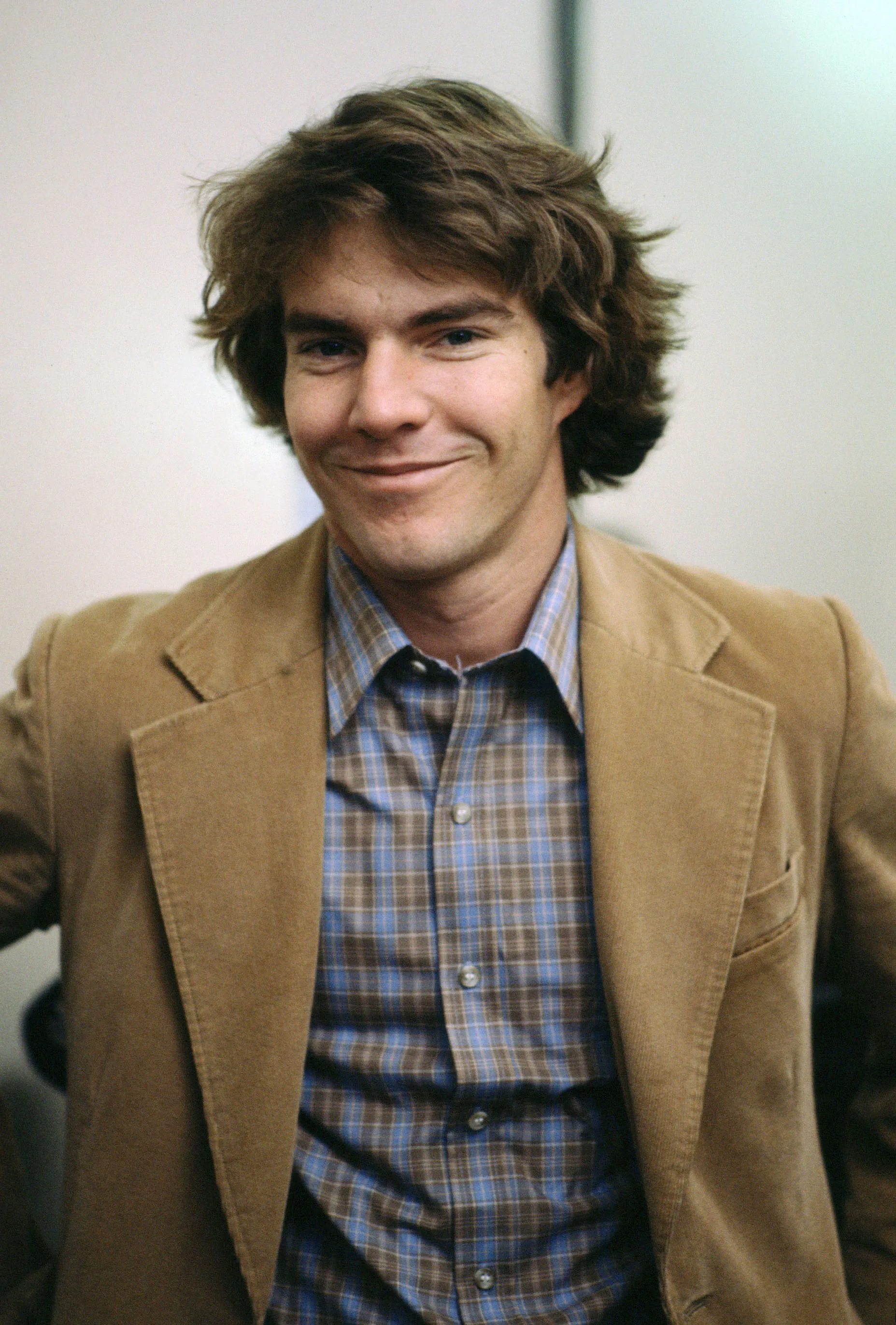 Actor Dennis Quaid smiling in a tan corduroy jacket and blue plaid shirt.
