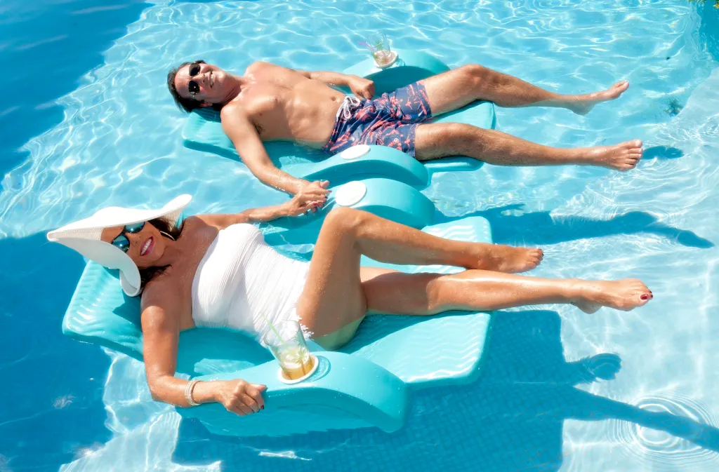 Actress Joan Collins reclines on a floating armchair in a pool with her husband Percy Gibson.