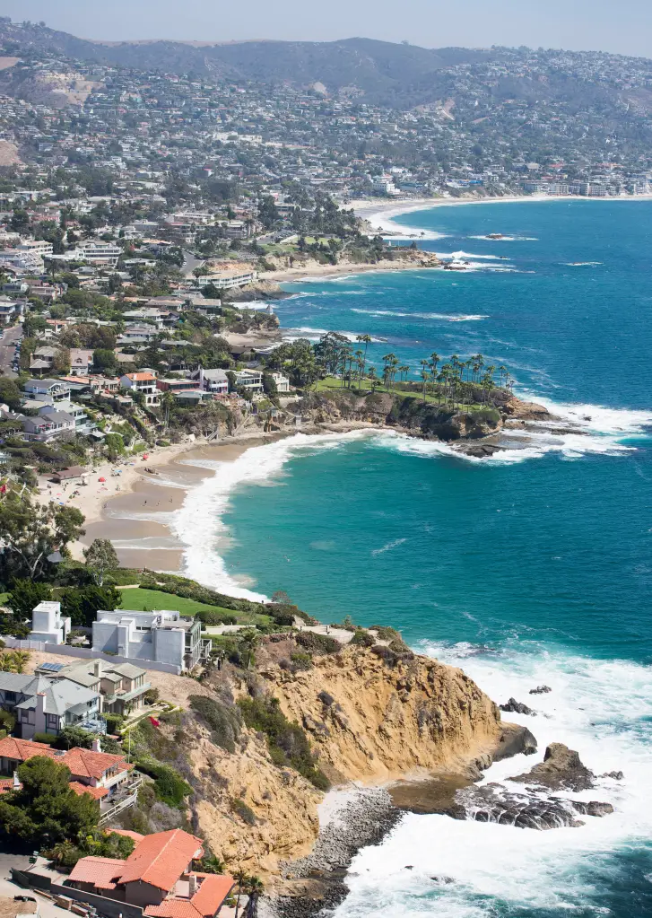 Aerial photo of houses along the Laguna Beach coastline, with hills in the background.