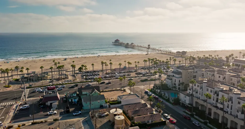 Aerial shot of the coastline at Huntington Beach, California, with the pier extending into the ocean and palm trees lining the beach.