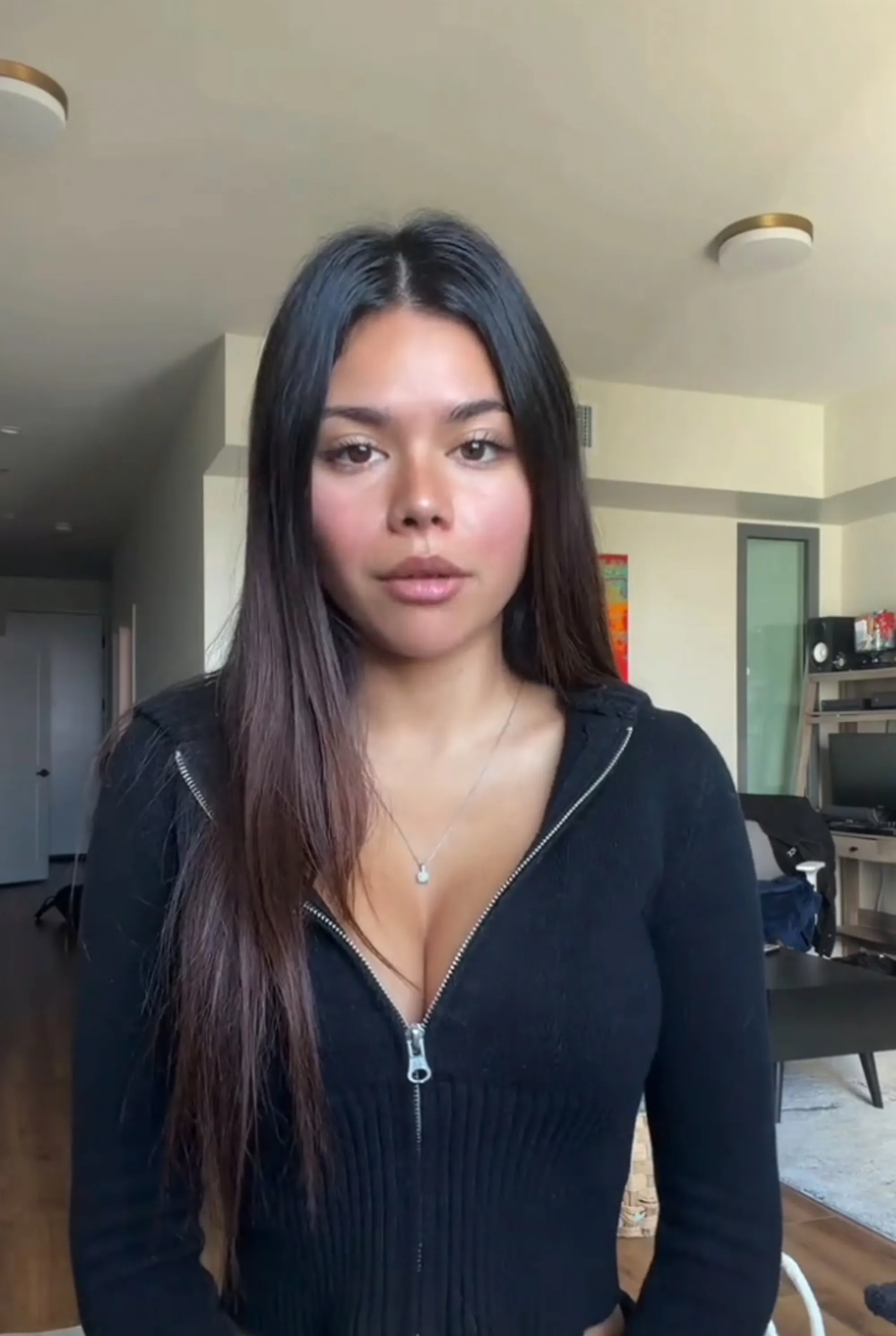 Alannah Keyser in a video, wearing a black long-sleeved zipped top and a necklace, with a worried expression.