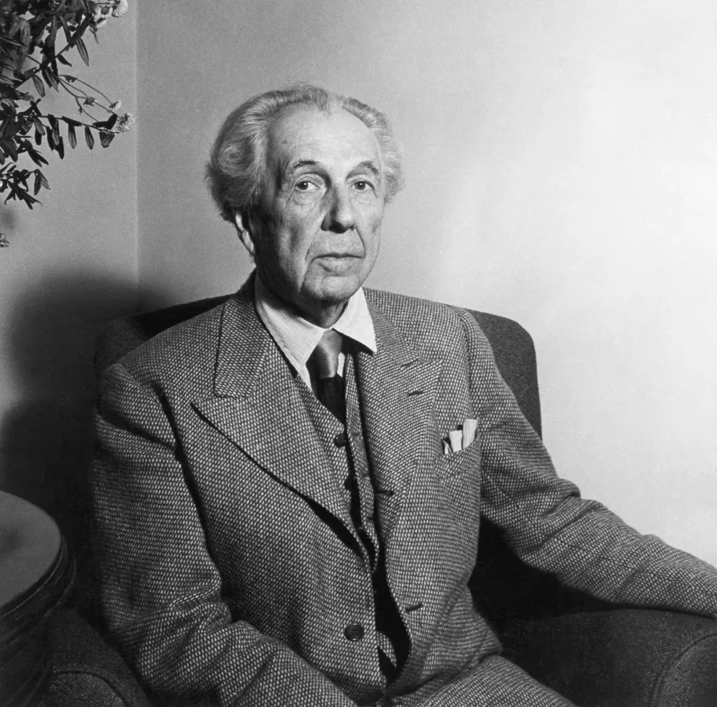 Half-length portrait of American architect Frank Lloyd Wright at age 77, sitting in a chair, wearing a suit and tie.
