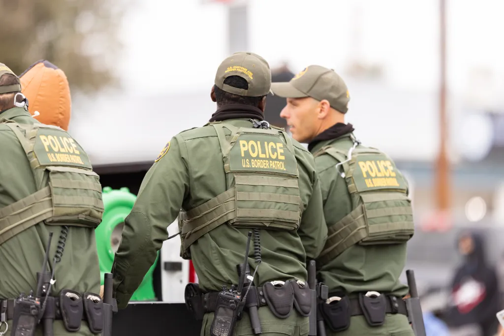 Three members of the U.S. Border Patrol, wearing green uniforms, hats, and vests with 