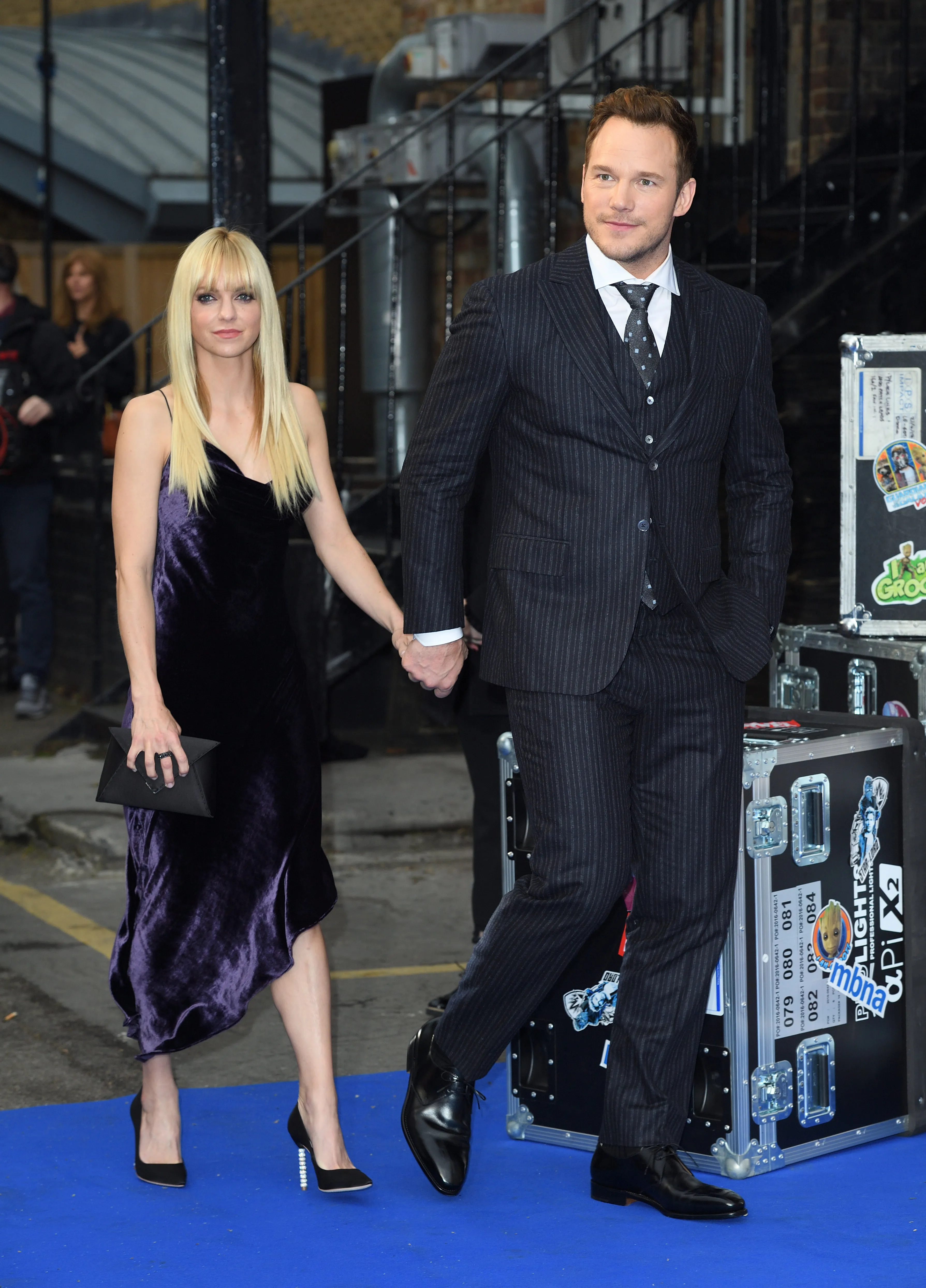 Anna Faris in a purple dress and Chris Pratt in a pinstripe suit holding hands.