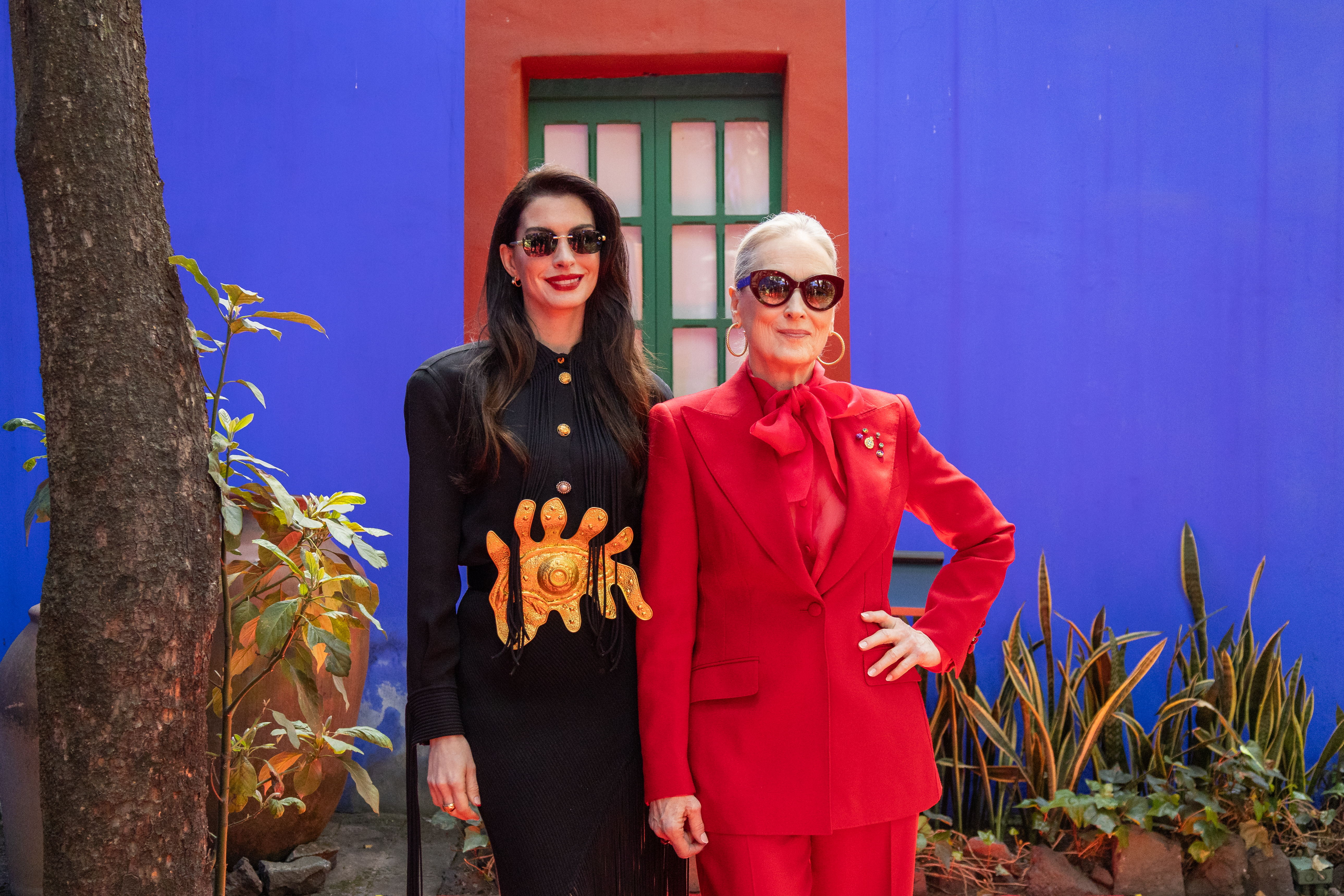 Anne Hathaway and Meryl Streep pose together against a blue wall with a red-orange window frame.