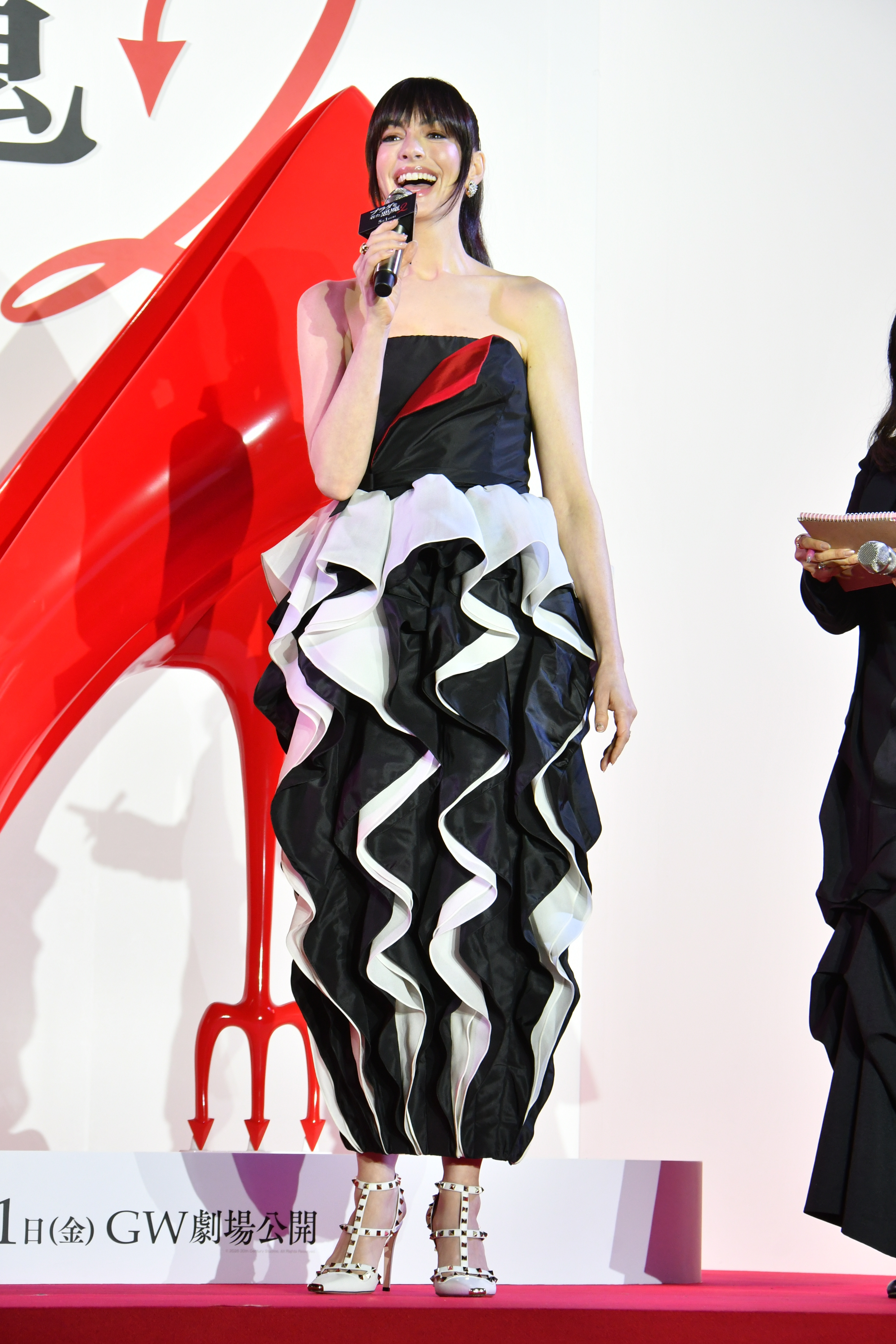 Anne Hathaway speaking into a microphone at The Devil Wears Prada 2 premiere in Tokyo.
