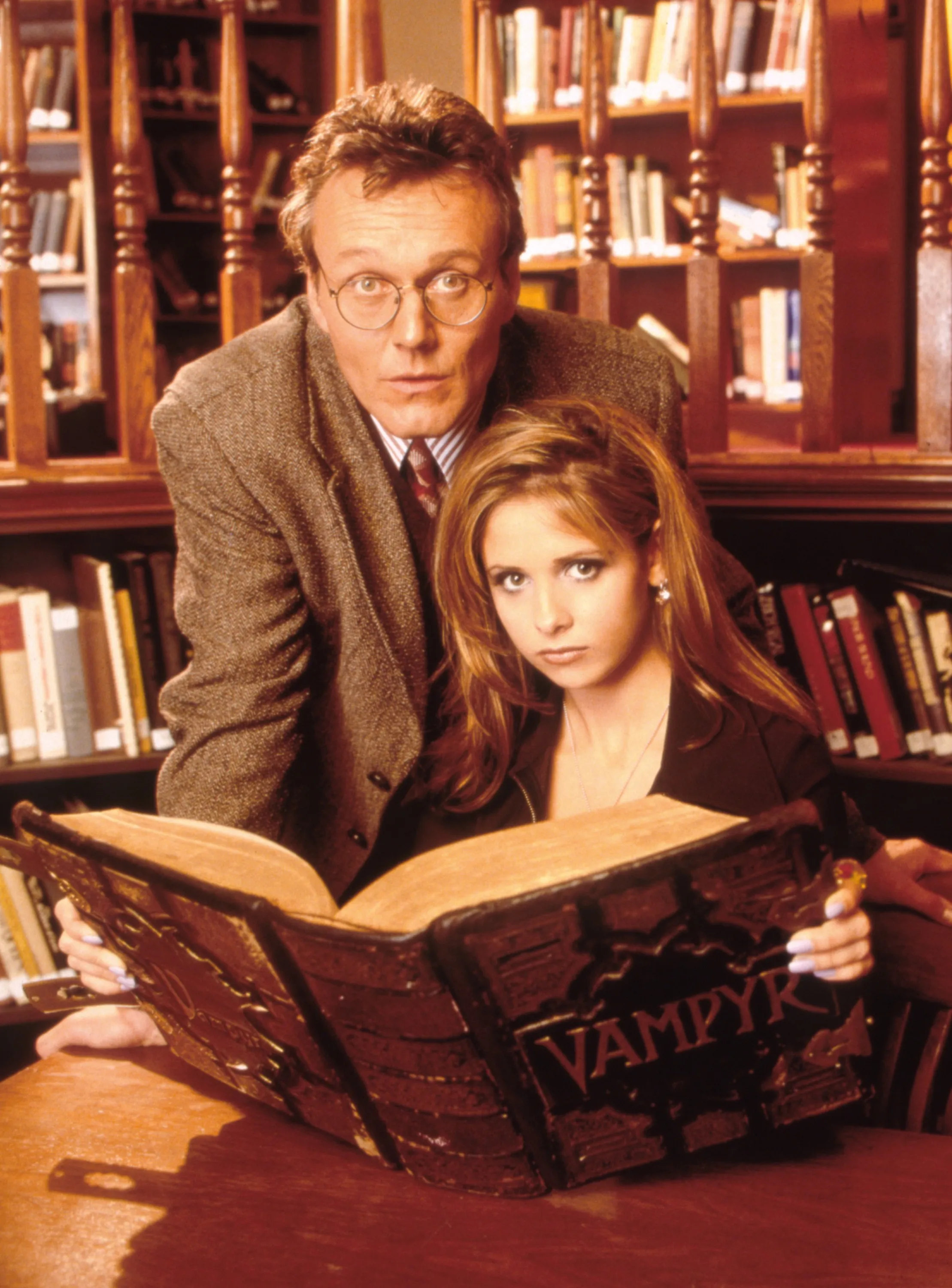 Anthony Stewart Head and Sarah Michelle Gellar looking at a book titled 