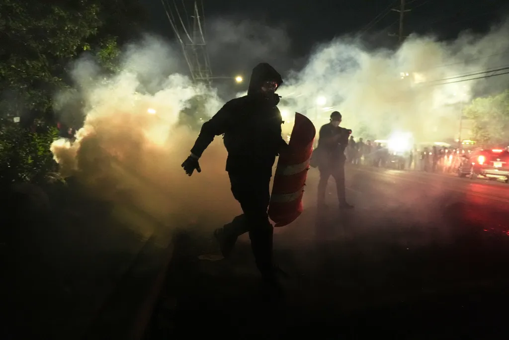 A masked protester with a makeshift shield runs through tear gas during clashes with law enforcement.