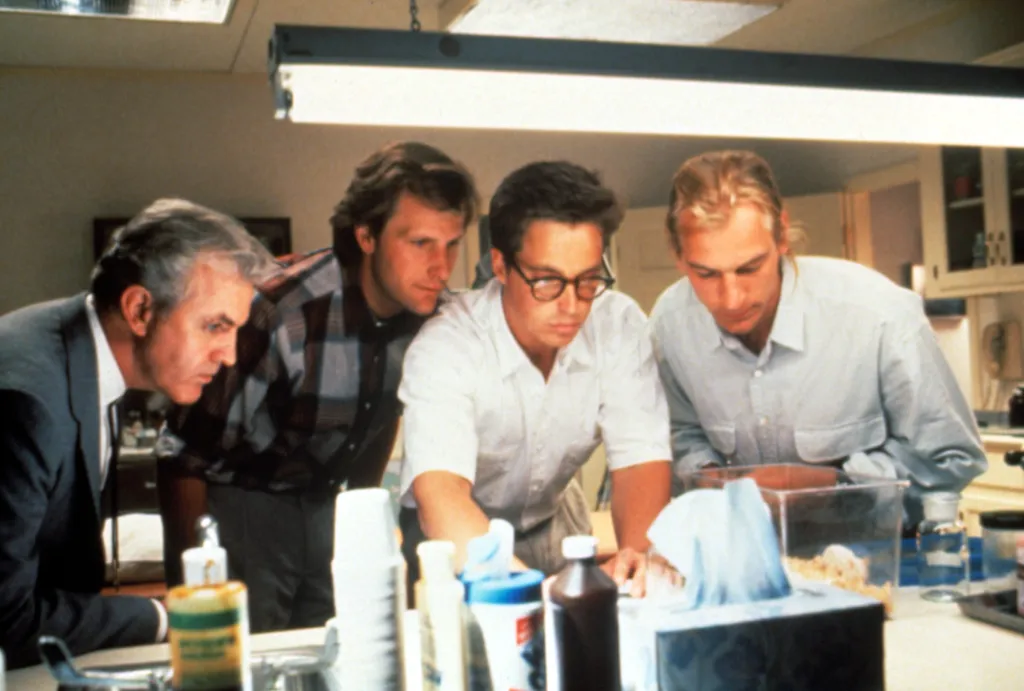 Four men look down at a small container with something inside.