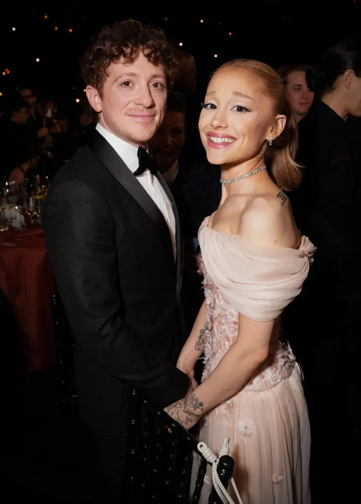 Ethan Slater, in a black tuxedo, and Ariana Grande in an off-the-shoulder pink dress, smiling.
