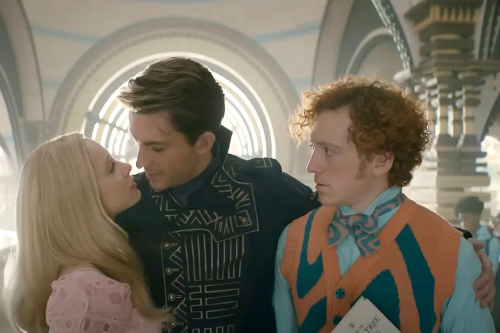 Ariana Grande, in a pink dress,Jonathan Bailey, in a black and white shirt, and Ethan Slater in an orange and green vest, and green shirt and orange and green tie, in a scene from the film 