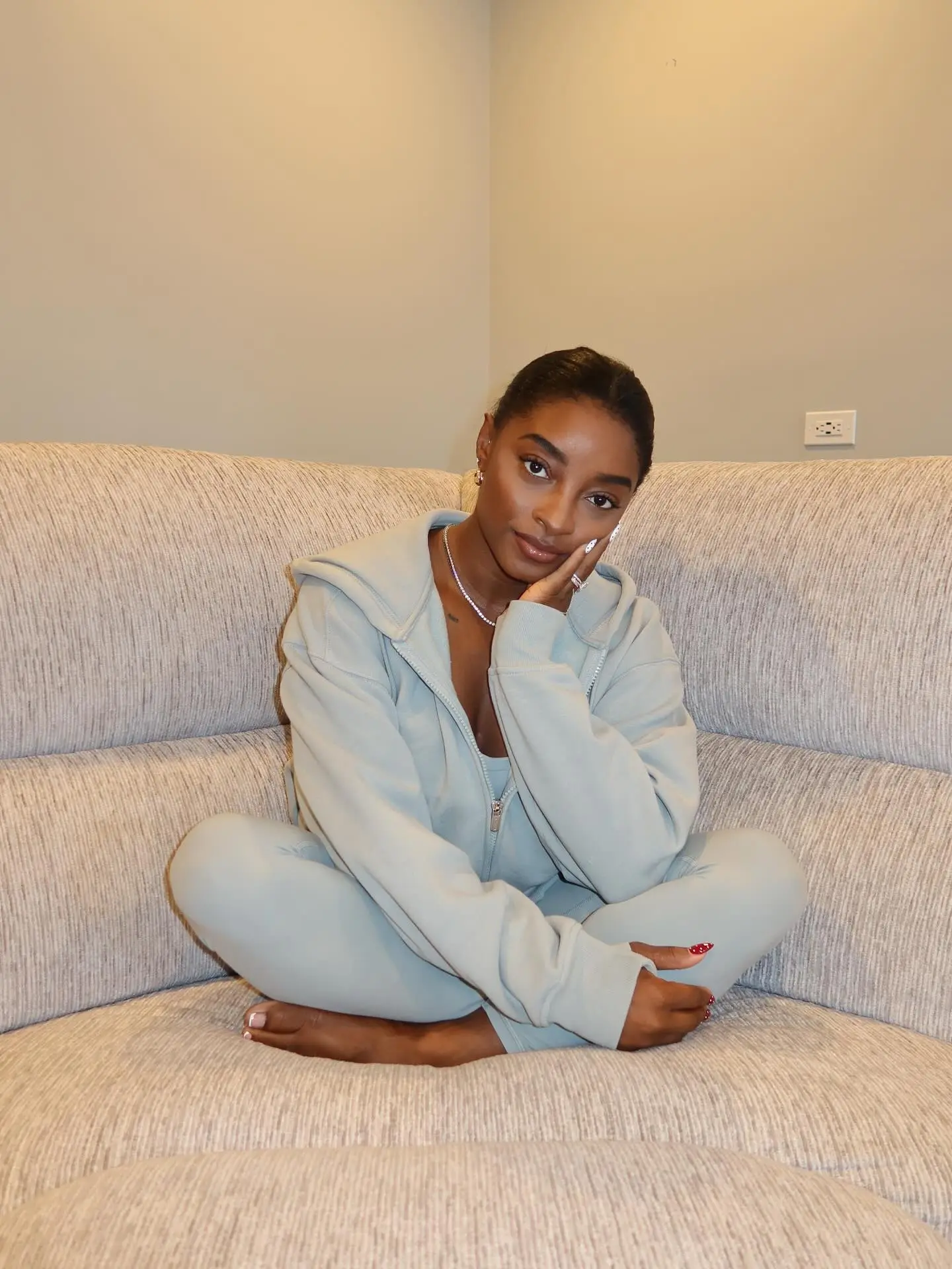 Simone Biles modeling an Athleta studio set while sitting on a couch.