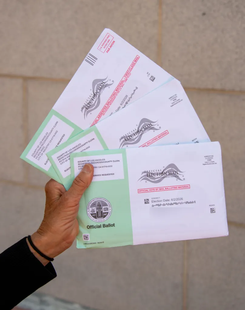 A hand holding several official ballot envelopes marked for election mail, with 