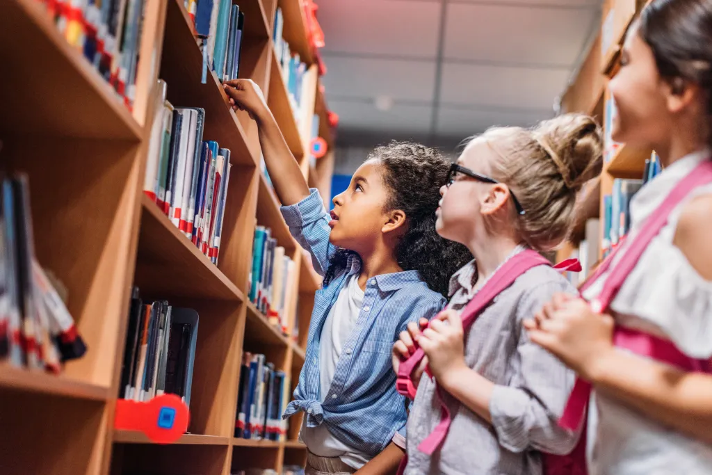 Three multiethnic schoolgirls looking for books in a library.