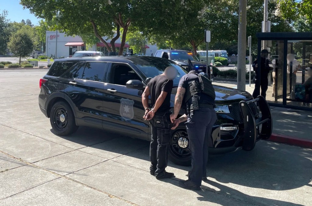 Berkeley police officer arresting Damarcus Jones near a police vehicle.