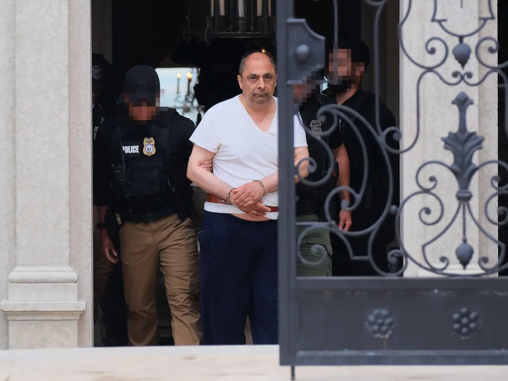 Jamshid Ghomi being arrested and led out of his home in handcuffs by law enforcement officers.