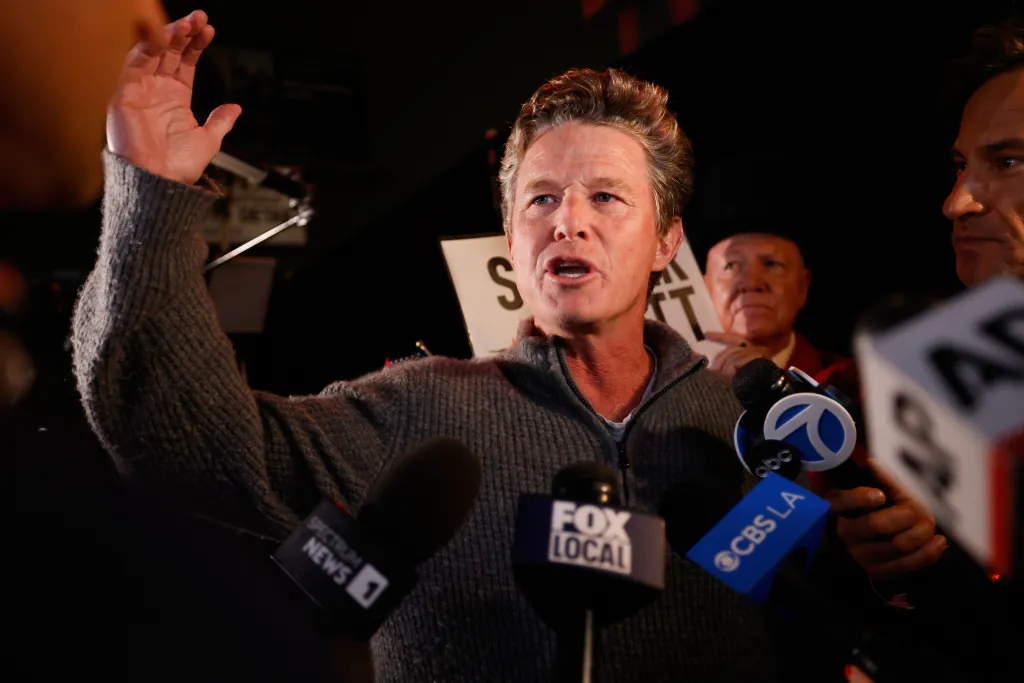 Billy Bush speaking outside an election night event, with microphones from various news outlets in front of him.