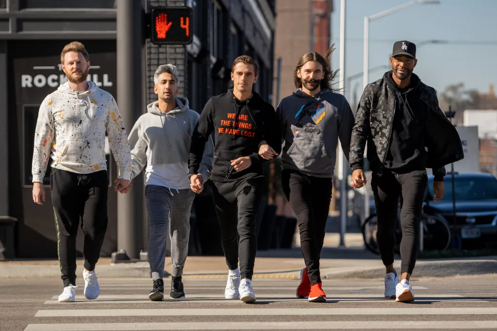 Cast shot of the Queer Eye Fab Five walking hand-in-hand across a crosswalk.