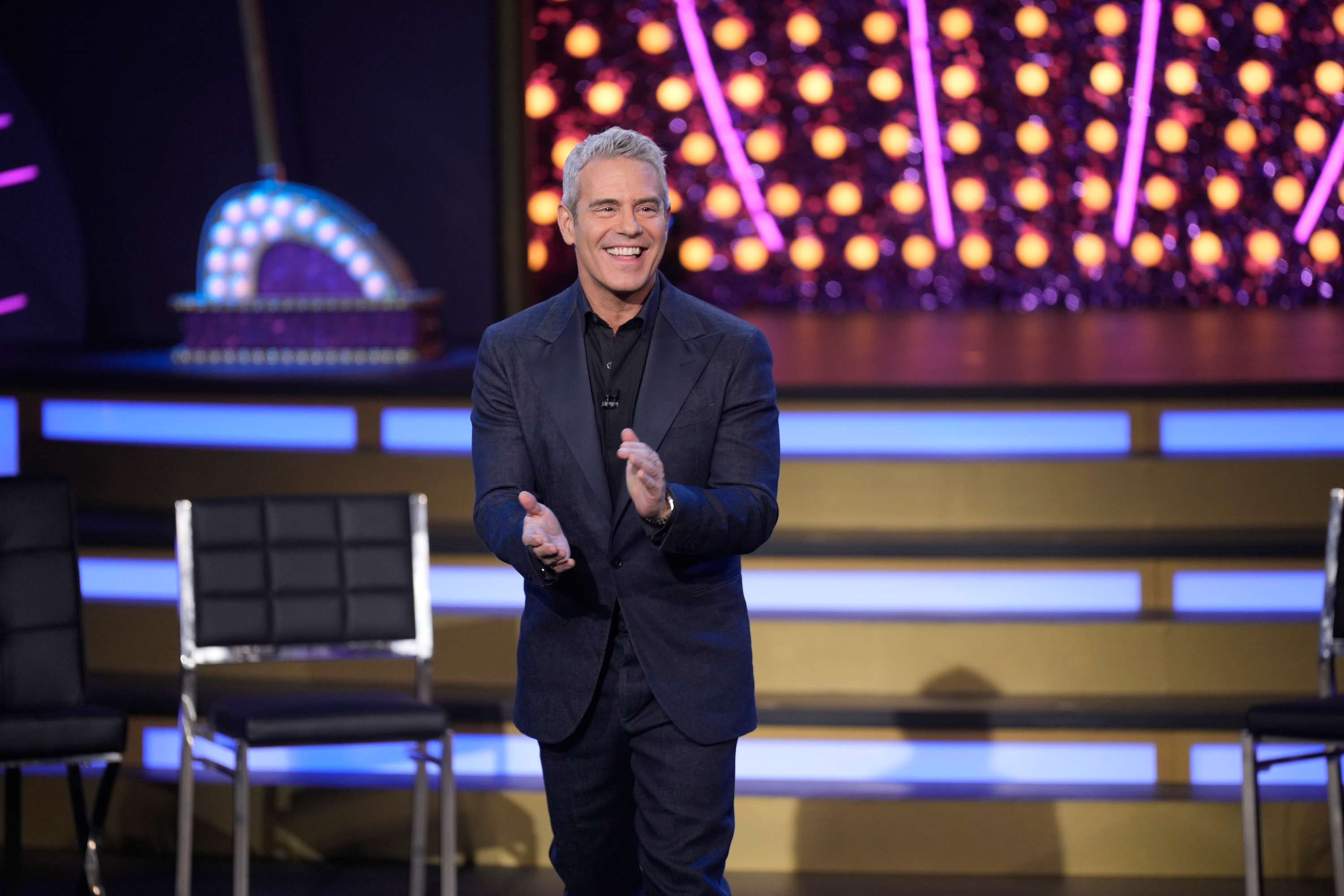 Andy Cohen smiling and clapping on stage.