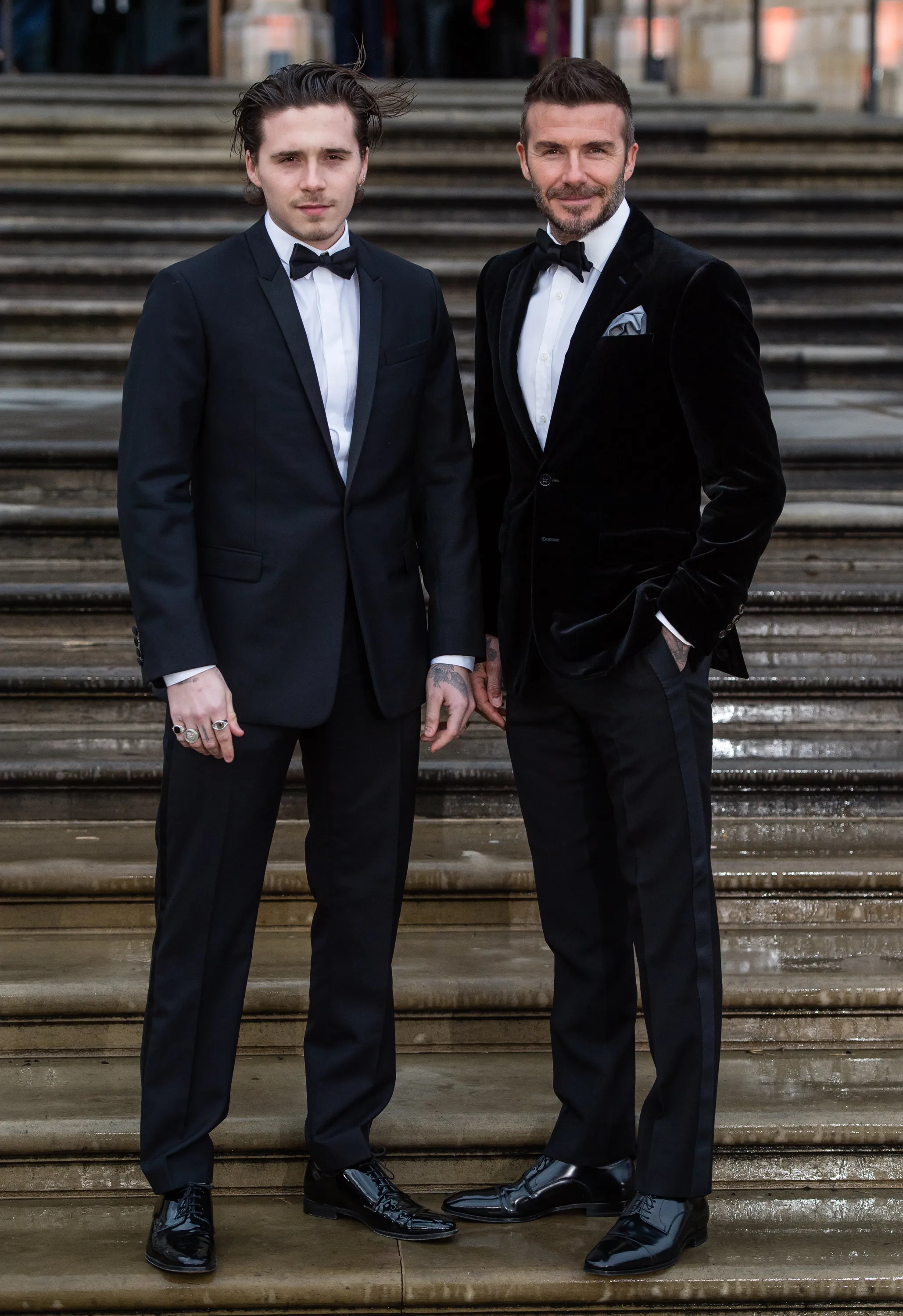 Brooklyn and David Beckham standing together on stairs in formal attire.
