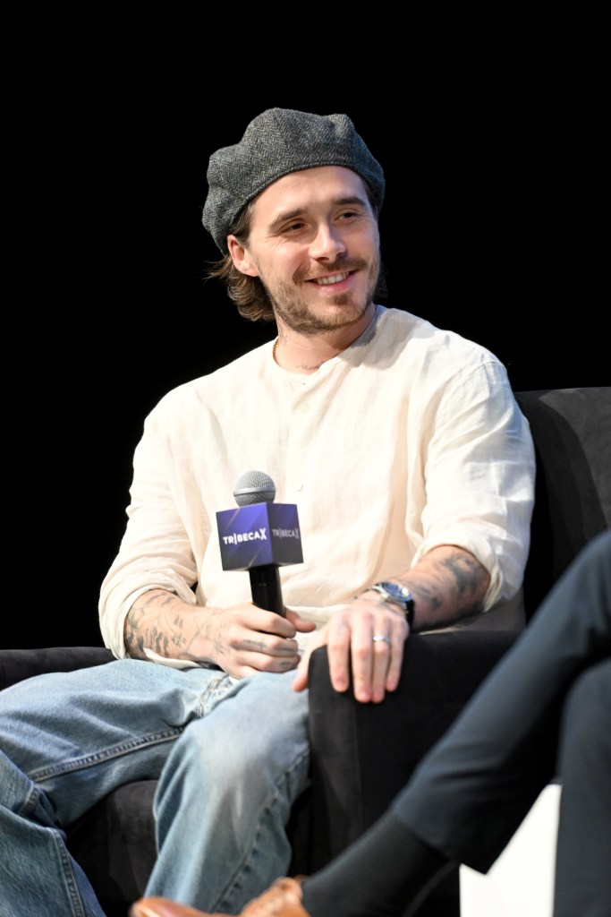 Brooklyn Beckham, in a cream top, blue jeans and grey hat, speaking at Tribeca X - 2026 Tribeca Festival.