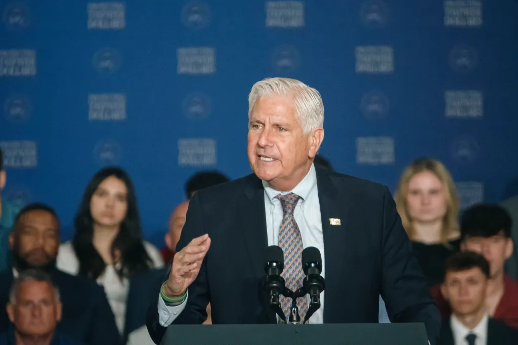 Bruce Blakeman, 10th County Executive of Nassau County, speaking at a podium with a blue background.