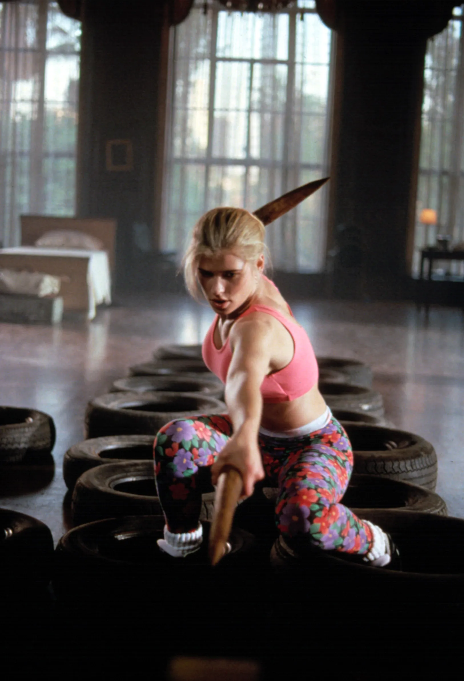 Kristy Swanson holding a wooden stake and kneeling among tires, training for her role in 