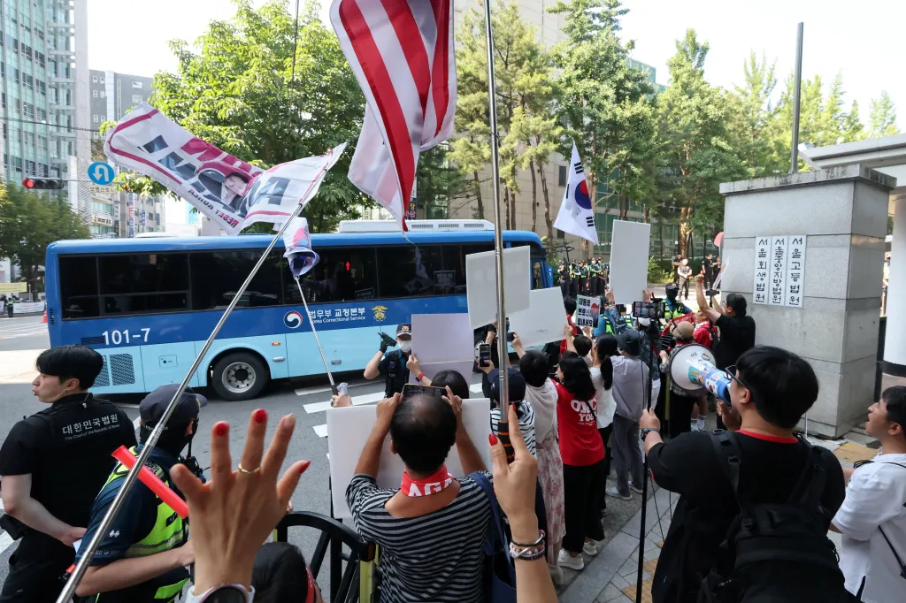 A bus carrying former South Korean President Yoon Suk Yeol arriving at the Seoul Central District Court for his sentencing trial, with protestors and security present.