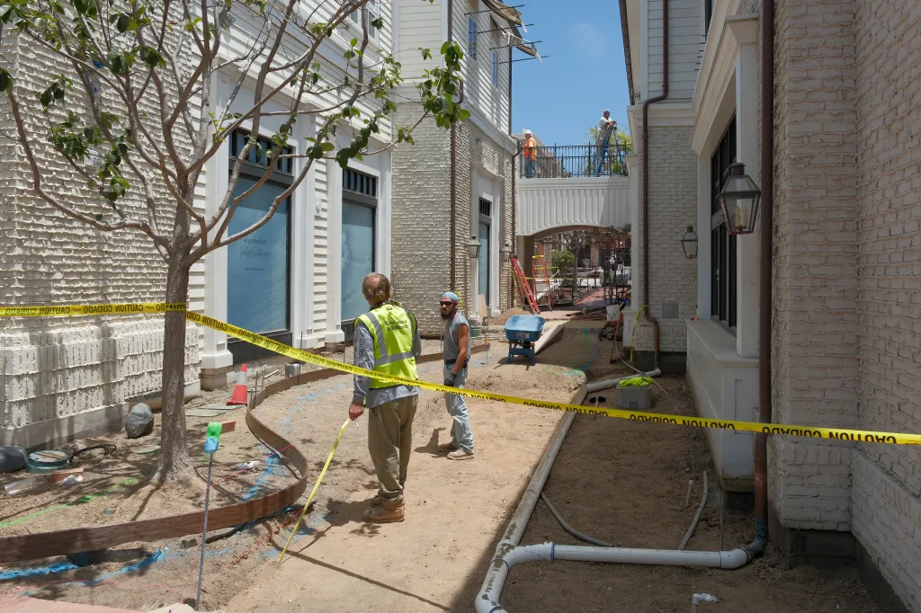 Construction workers stand on a dirt path with caution tape at Palisades Village.