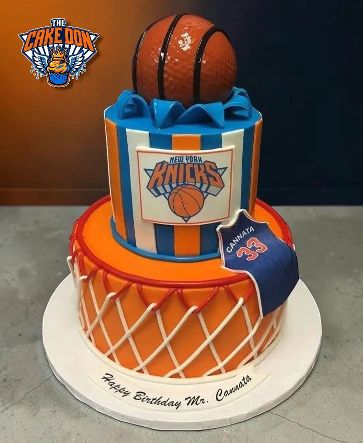 A two-tiered specialty cake decorated in the style of the New York Knicks, topped with a basketball and a jersey.