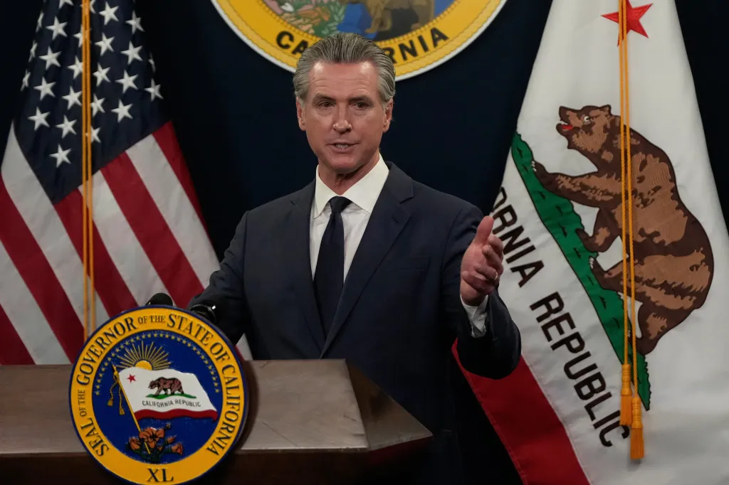 California Governor Gavin Newsom speaking at a podium with American and Californian flags behind him.