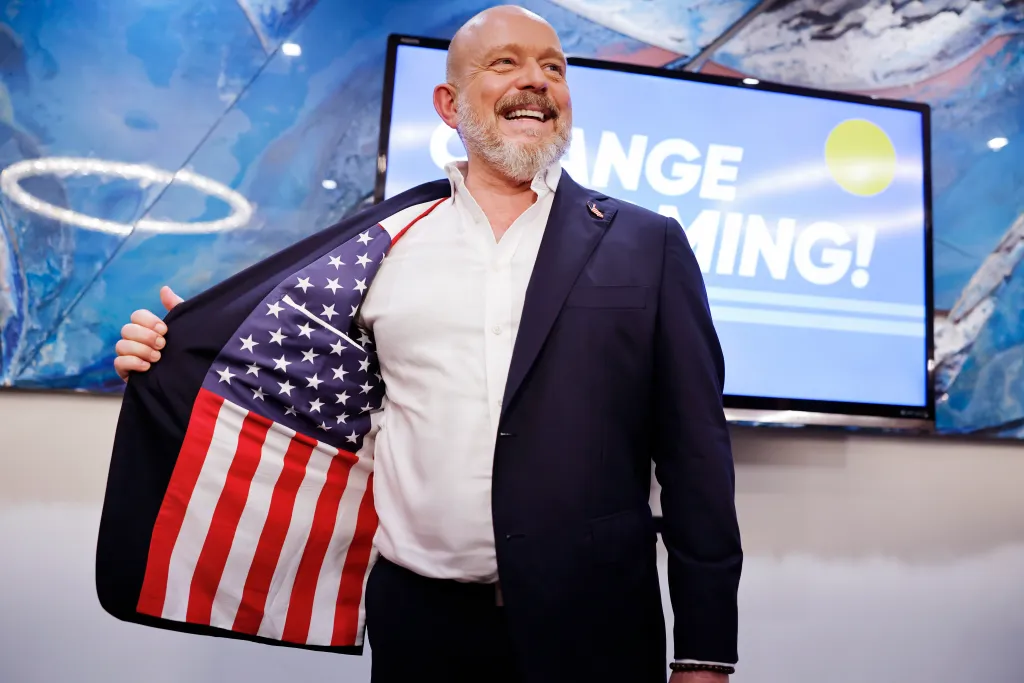 Steve Hilton smiles, revealing the American flag lining of his dark suit jacket.