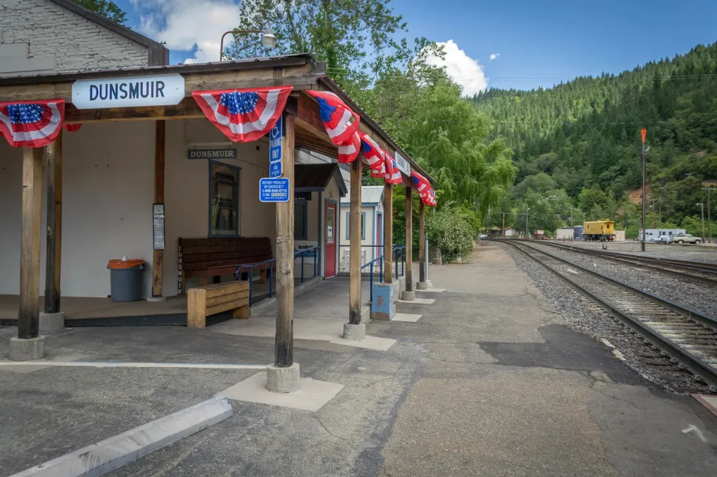 The Dunsmuir train station with red, white, and blue bunting, next to railroad tracks leading through a forested valley.