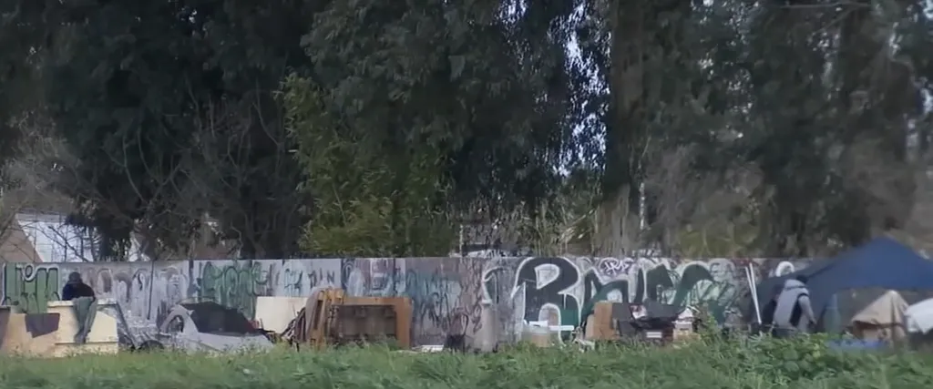 Encampments of unhoused people are set up against a graffiti-covered wall of the Cambodian Buddhist temple in Fresno County.