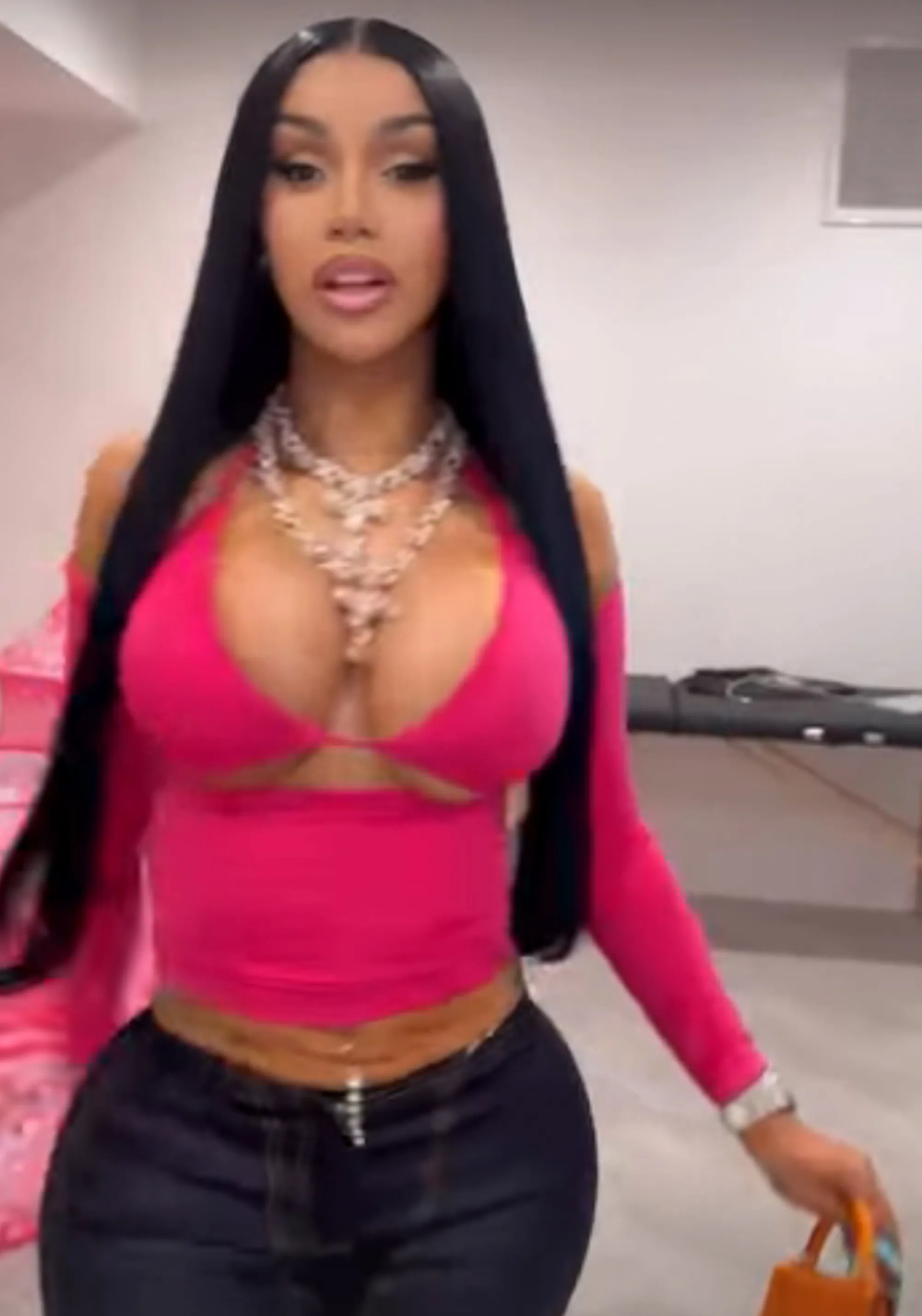 Cardi B in a pink cut-out top, jeans, and necklaces.