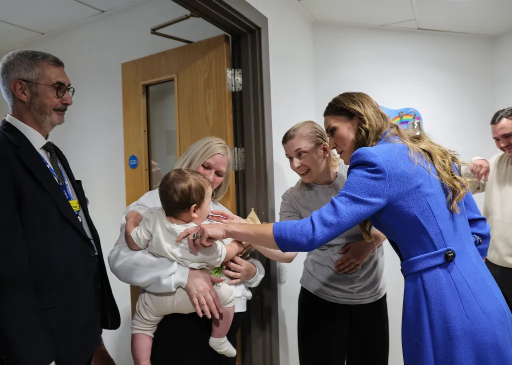 Catherine, Princess of Wales, engages with a baby held by a woman during her visit to The Christie NHS Foundation Trust.