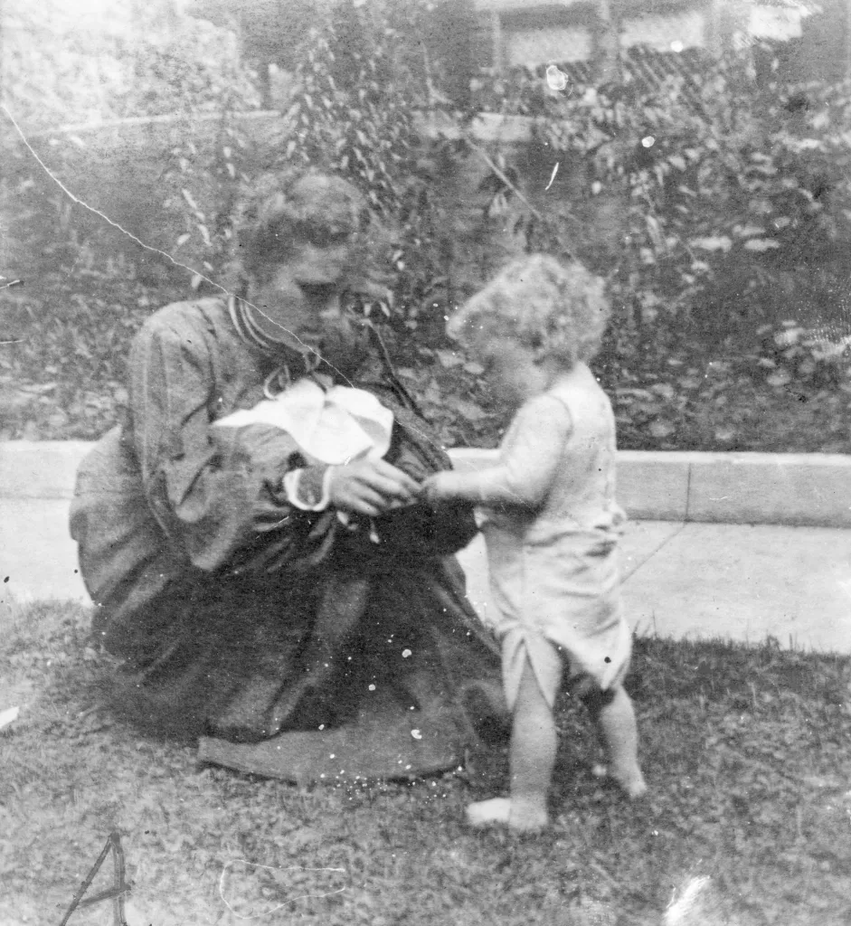 Catherine Tobin Wright kneeling and holding hands with Llewellyn Wright in front of their home.