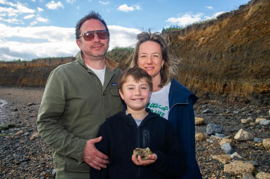 A boy holding an ancient elephant tooth poses with his parents on a beach.
