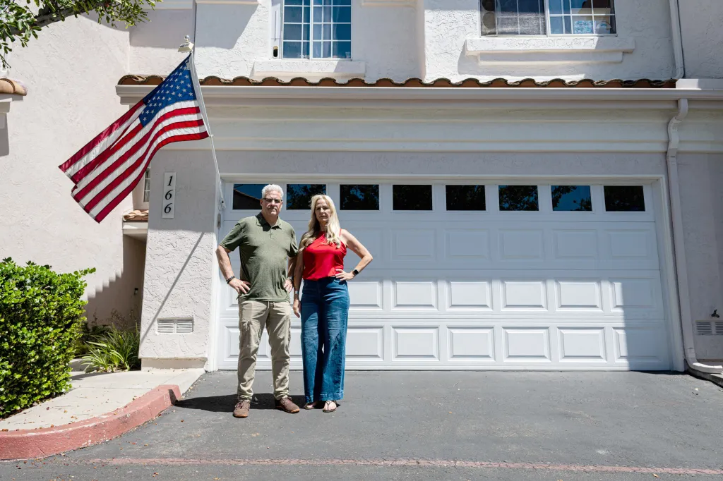 Chris and Amy Cooke stand beside their American flag displayed outside their San Marcos, CA home.