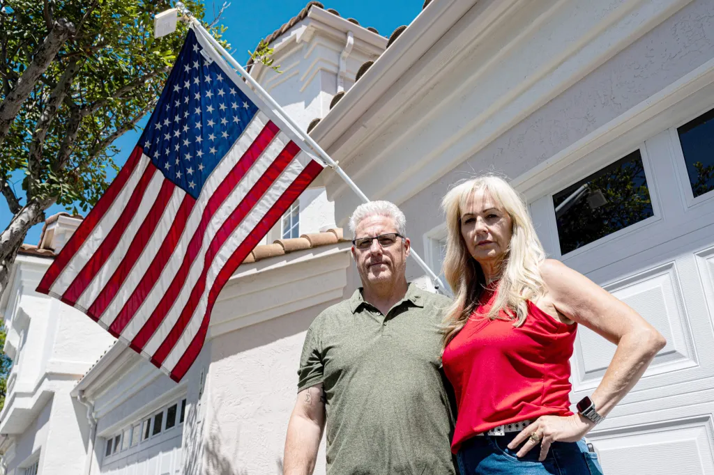 Chris and Amy Cooke standing in front of their home next to an American flag.