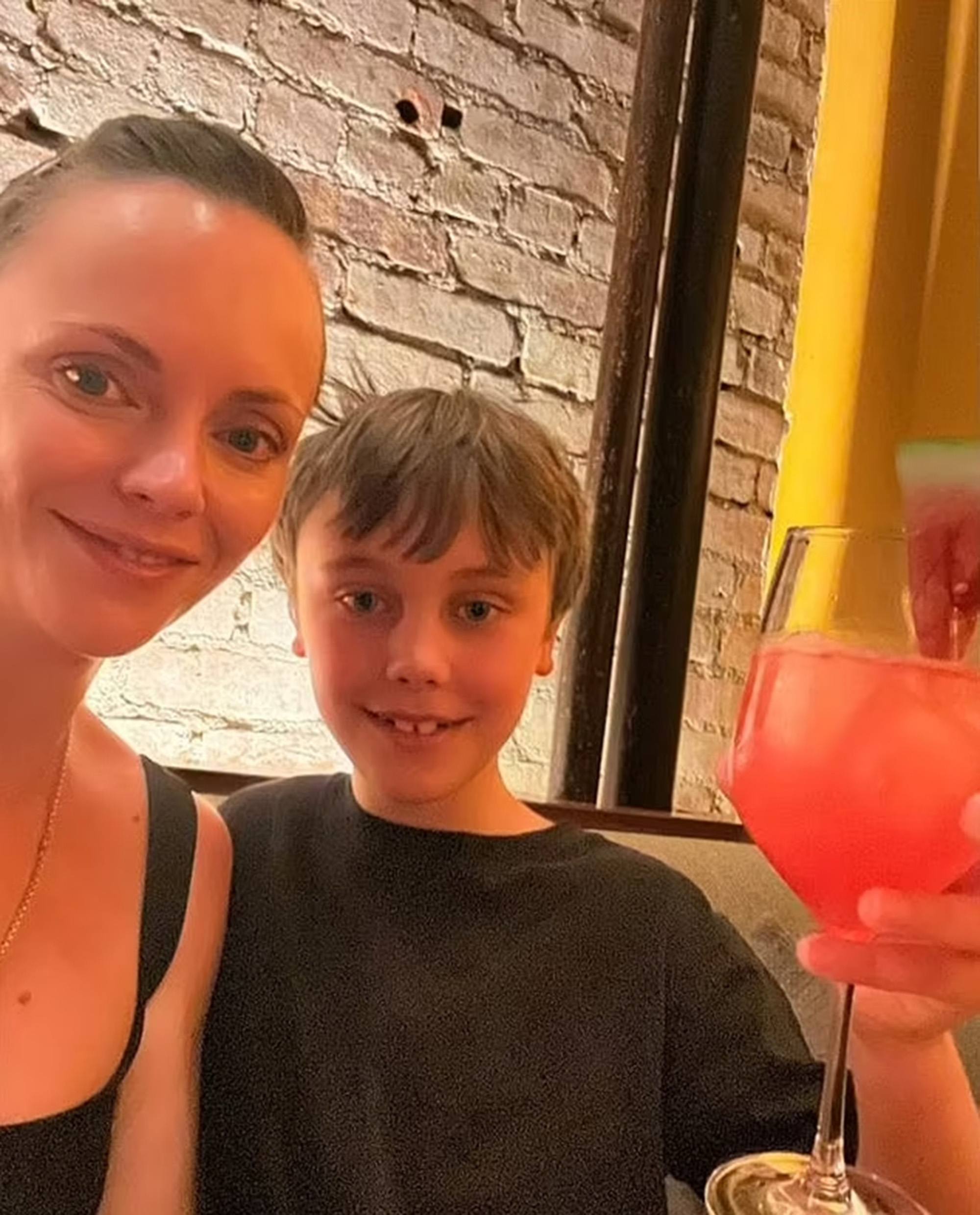 Christina Ricci smiling while her son holds a pink drink.