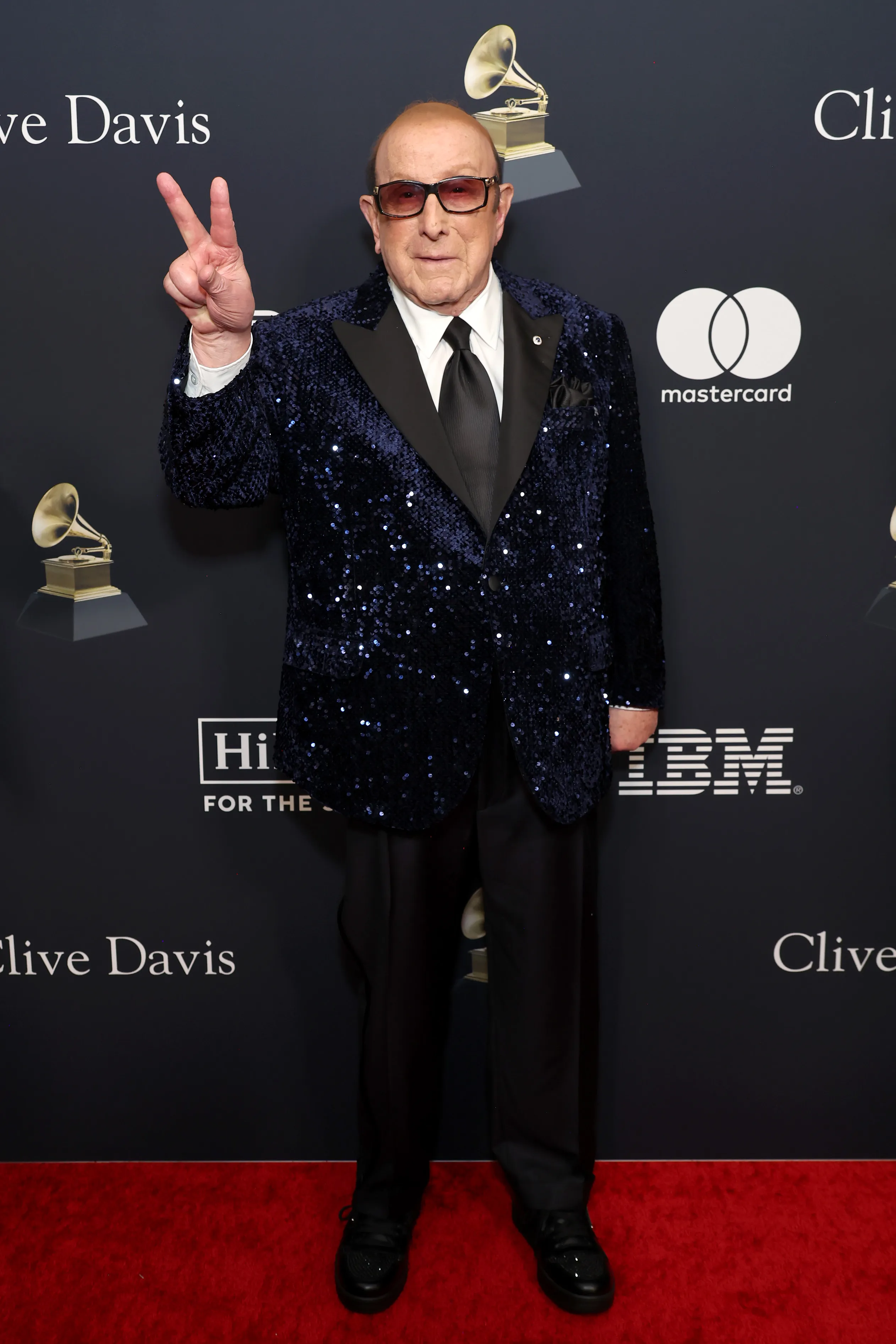 Clive Davis in a sequined blue jacket making a peace sign