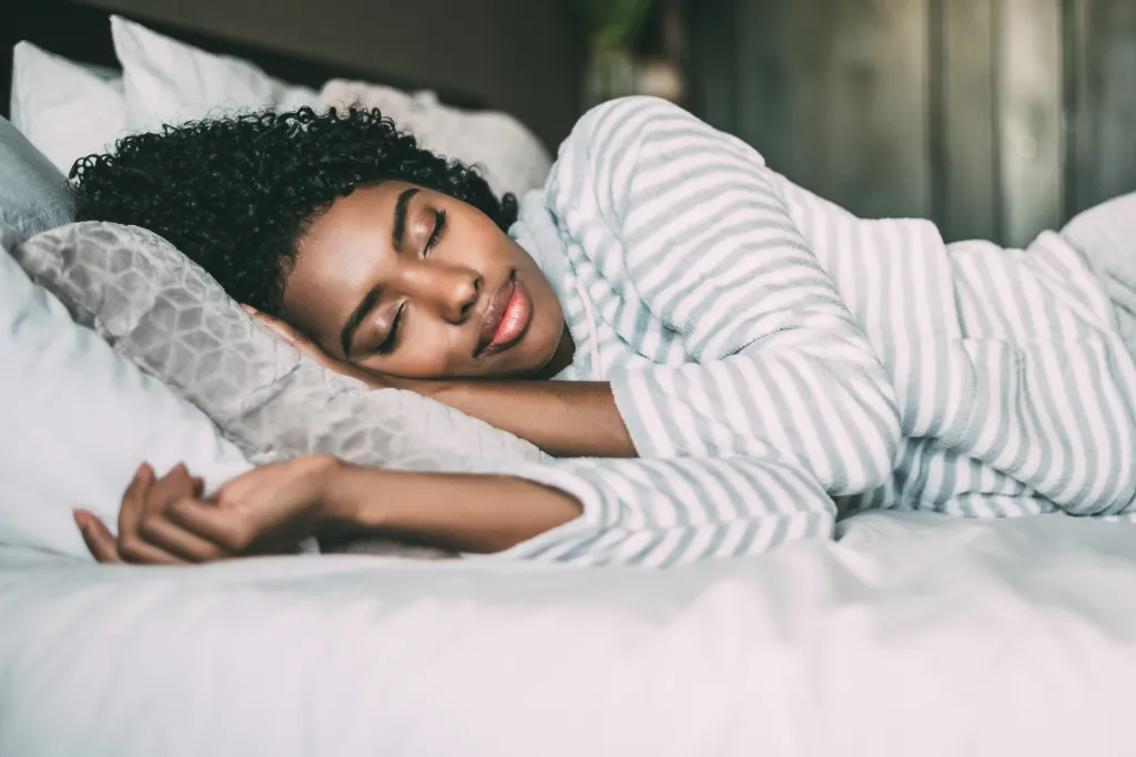 A pretty young Black woman with curly hair sleeping comfortably in bed.