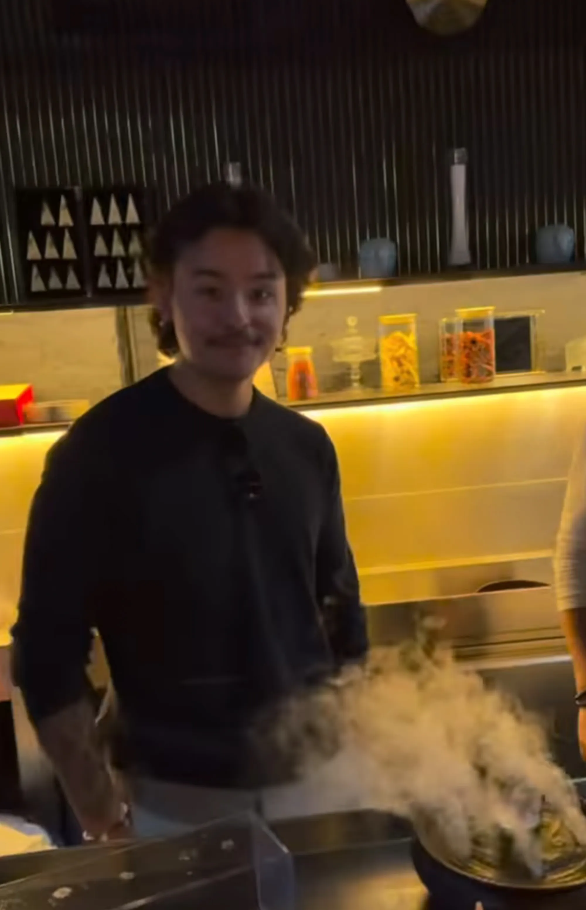 Collin Gosselin in a dark shirt standing near a counter with smoking food.