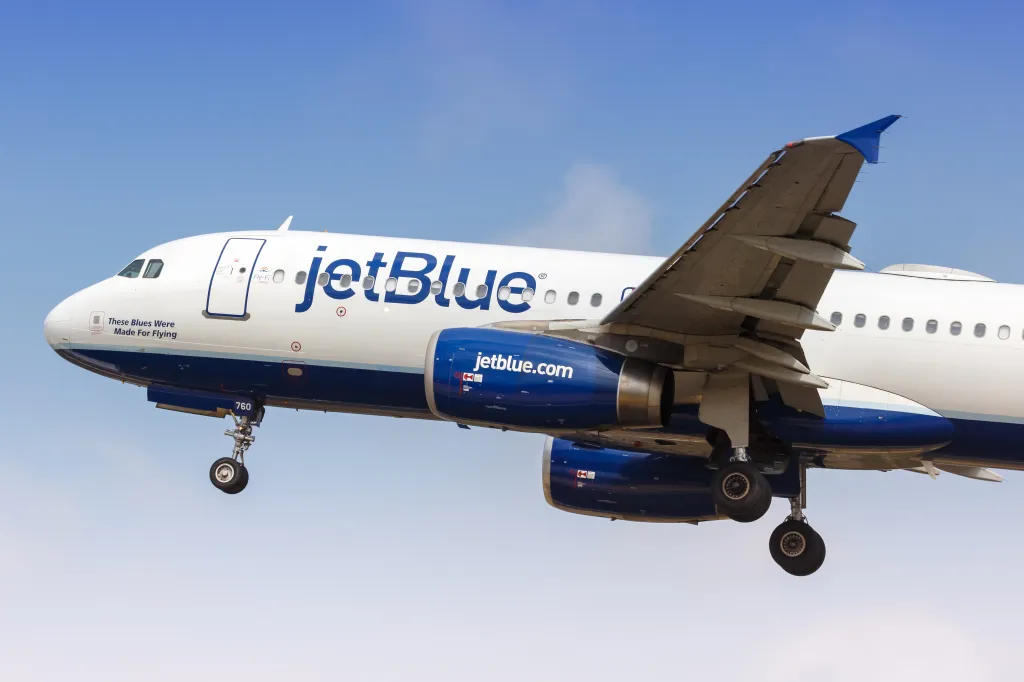 JetBlue Airbus A320 airplane with landing gear down and a blue tail winglet, flying through a clear sky.