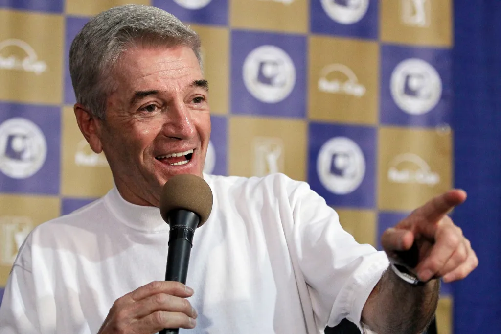 Comedian Tom Dreesen speaking into a microphone and pointing.