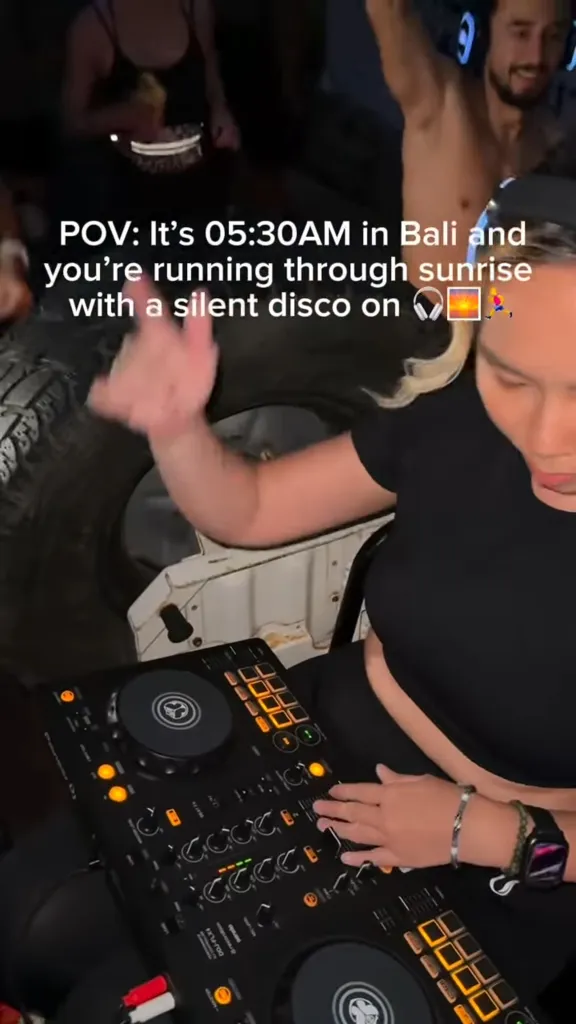 A person DJing in a moving vehicle with text overlaid describing a silent disco run in Bali.