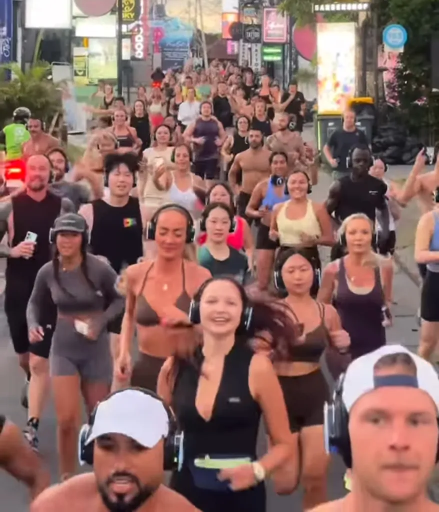 A large group of people wearing headphones running down a street with neon-lit buildings in the background.