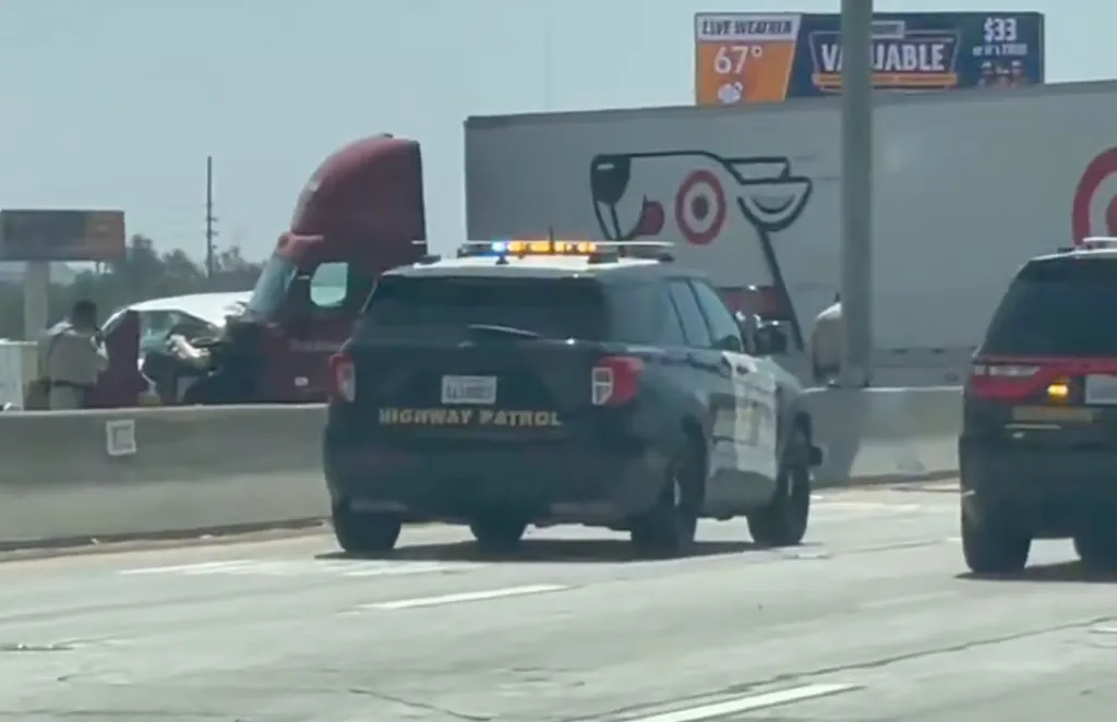 Police cars near a crashed semi-truck and trailer on the median of the 210 Freeway.
